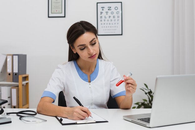 Doctor escribiendo un informe y sosteniendo una muestra de sangre