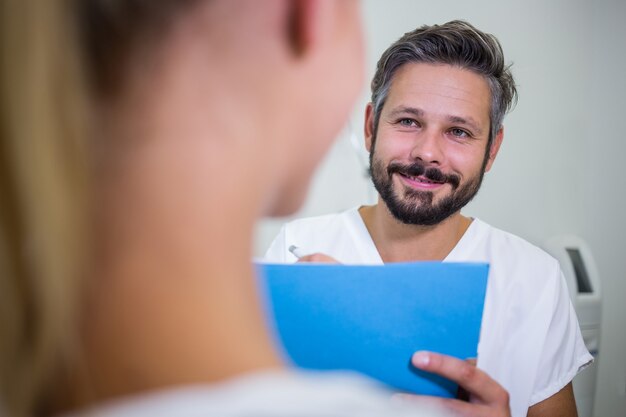 Doctor escribiendo en informes mientras discute con el paciente