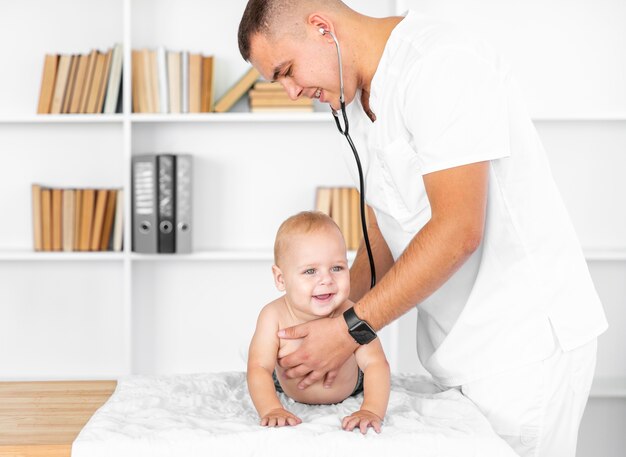 Doctor escuchando sonriente bebé con estetoscopio