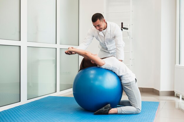 Doctor estirando paciente en pelota de ejercicios