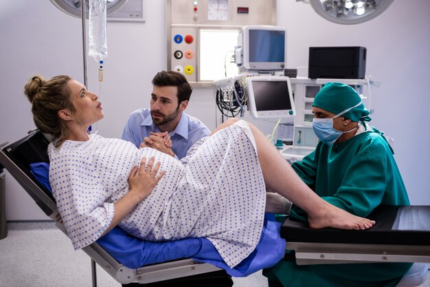 Doctor examinando a la mujer embarazada durante el parto mientras que el hombre de la mano