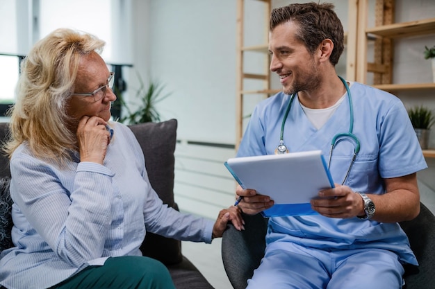 Doctor feliz comunicándose con una anciana sobre documentos médicos mientras está en una visita a casa