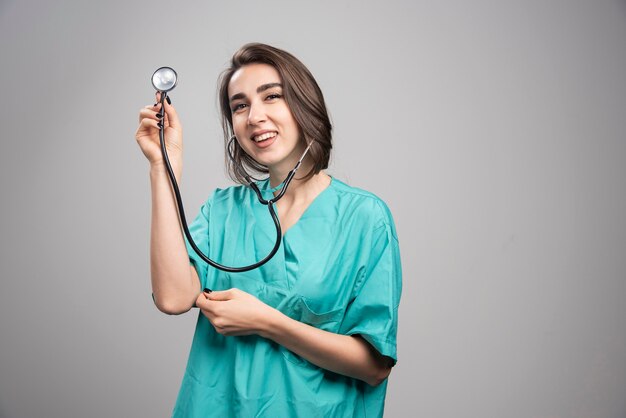 Doctor feliz que muestra el estetoscopio sobre fondo gris. Foto de alta calidad