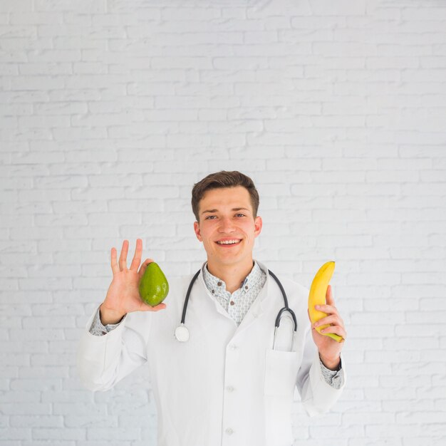 Doctor feliz que sostiene el aguacate y el plátano en manos