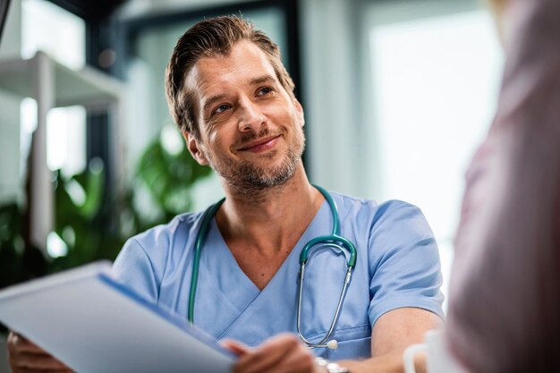 Doctor feliz sosteniendo papeleo médico mientras se comunica con el paciente durante la cita médica en el hospital