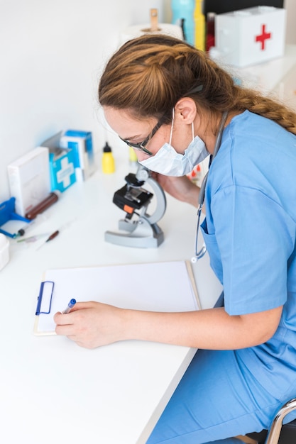 Doctor femenino usando máscara escribiendo en el portapapeles en un laboratorio