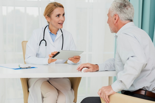 Doctor hablando con el paciente mientras sostiene la tableta