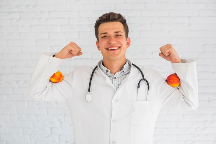 Foto gratuito doctor hombre flexionando sus manos sosteniendo manzanas rojas en su bíceps