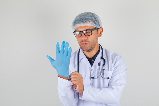 Doctor hombre ponerse guantes en bata blanca médica