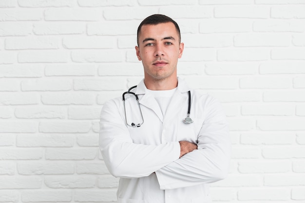 Foto gratuita doctor hombre posando delante de la pared de ladrillos blancos