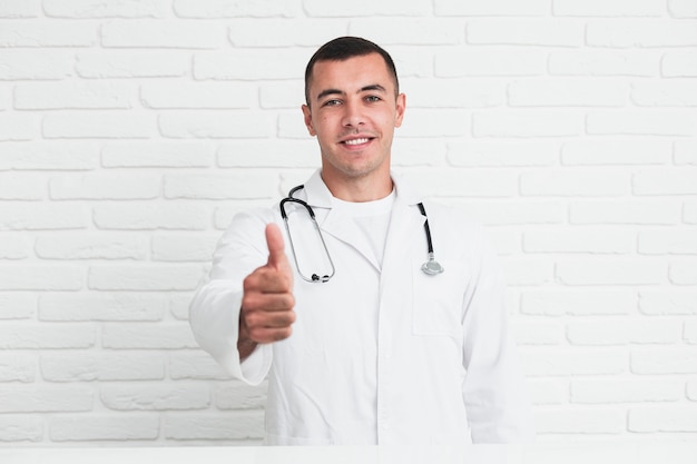 Doctor hombre sonriente posando delante de la pared de ladrillos blancos