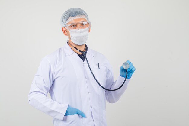 Doctor hombre sosteniendo estetoscopio y mirando a la cámara en ropa protectora