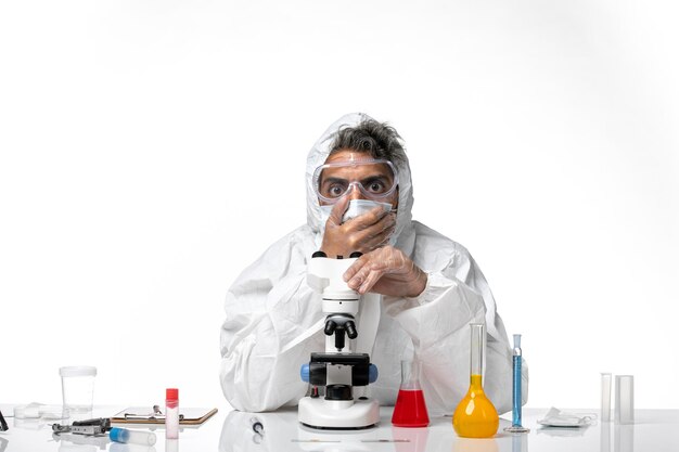 Doctor hombre en traje de protección y máscara sentado en blanco