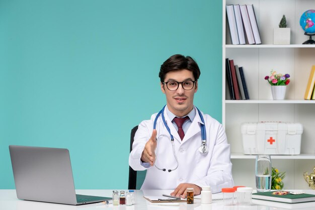 Doctor inteligente lindo serio médico en bata de laboratorio trabajando de forma remota en la computadora dando apretón de manos