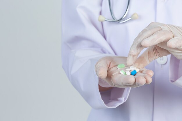 El doctor joven hermoso lleva la máscara mientras que sostiene la medicina con los guantes de goma en la pared gris.