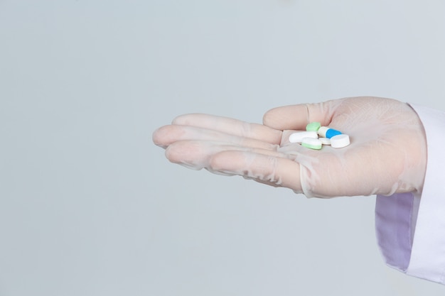 Foto gratuita el doctor joven hermoso lleva la máscara mientras que sostiene la medicina con los guantes de goma en la pared gris.