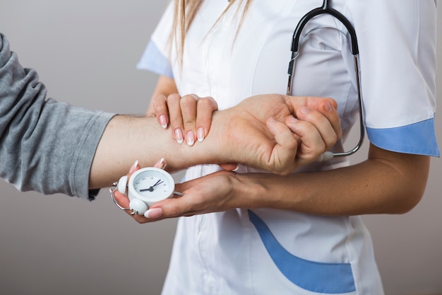 Doctor manos sosteniendo un reloj y mano paciente