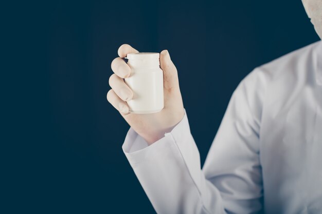 Doctor con máscara y guantes sosteniendo un frasco de pastillas en la vista lateral de la mano