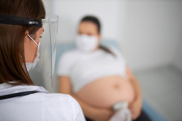 Doctor en máscara haciendo chequeo de ultrasonido para mujer embarazada