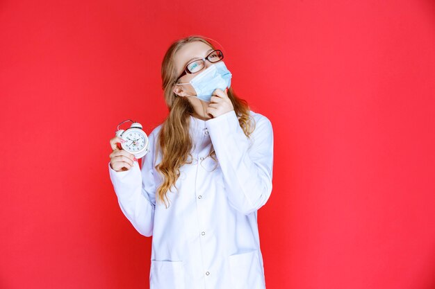 Doctor en mascarilla sosteniendo un reloj y parece confundido.