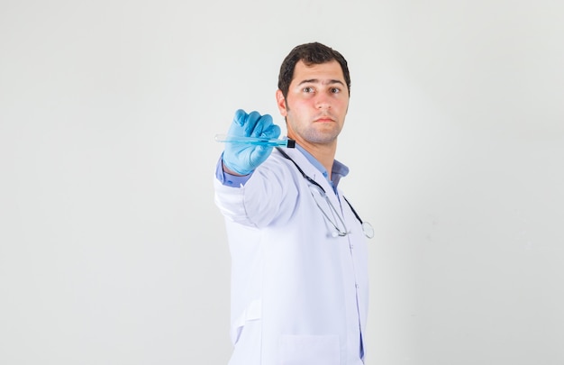 Doctor masculino en bata blanca, guantes apuntando tubo de ensayo a la cámara y mirando serio