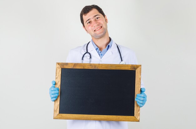 Doctor masculino en bata blanca, guantes sosteniendo la pizarra y mirando alegre