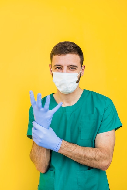 Doctor masculino en máscara poniéndose guantes estériles