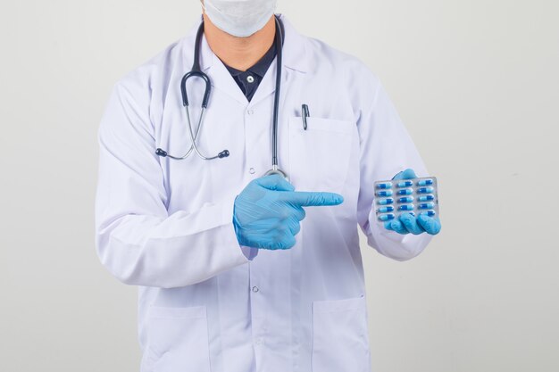 Doctor masculino mostrando paquete de cápsulas en bata blanca y máscara