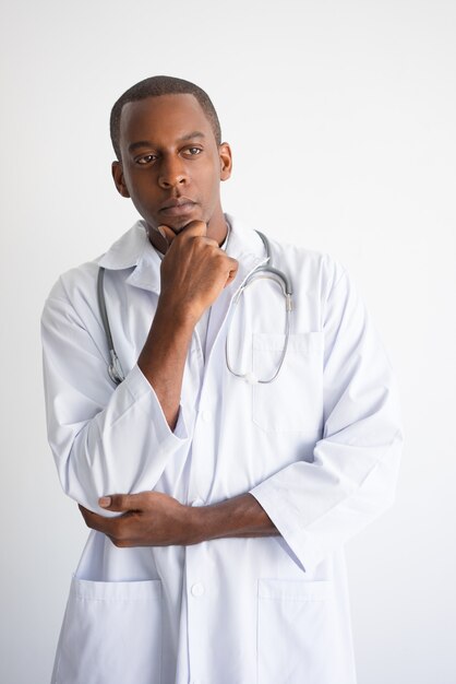 Doctor masculino negro pensativo que toca la barbilla. Concepto de decisión médica.