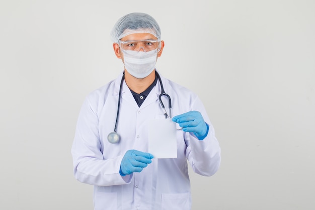 Doctor masculino en ropa protectora con tarjeta de papel blanco y mirando cuidado