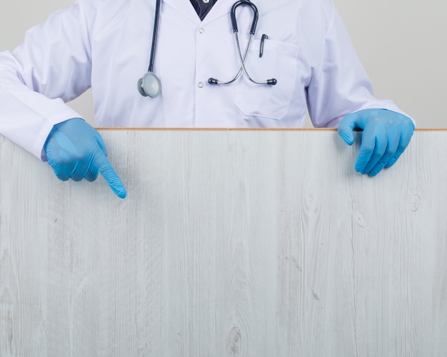 Doctor mostrando tablero de madera en bata blanca y guantes