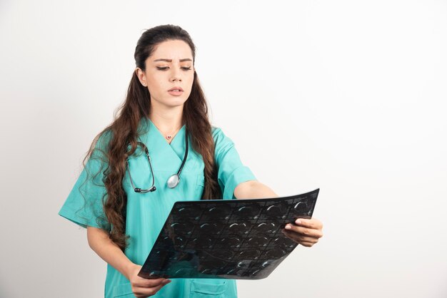 Doctor de la mujer joven que mira la radiografía sobre la pared blanca.