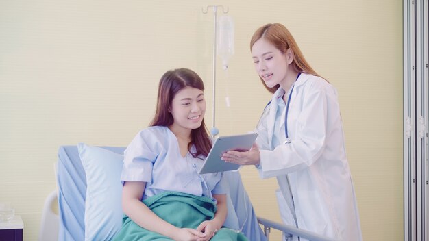 Doctor y paciente asiáticos elegantes hermosos que discuten y que explican algo con la tableta