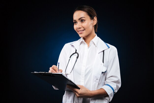 Doctor positivo joven escribiendo en portapapeles y mirando a un lado