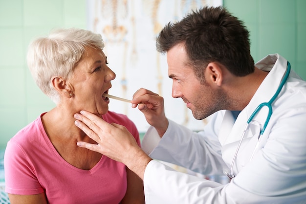 Doctor revisando la garganta de la mujer mayor