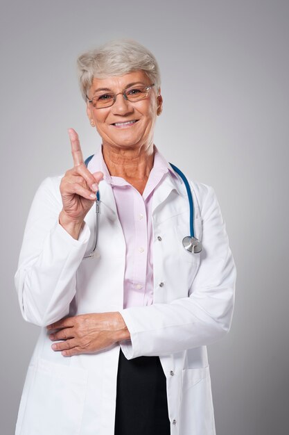 Doctor senior sonriente apuntando con el dedo