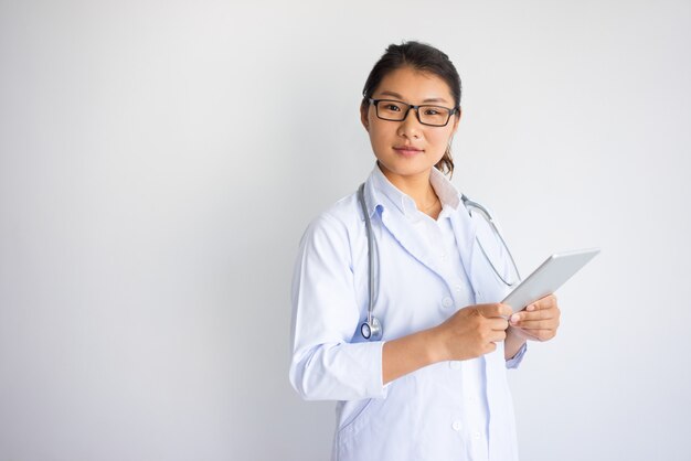 Doctor de sexo femenino joven asiático serio que usa la tableta.