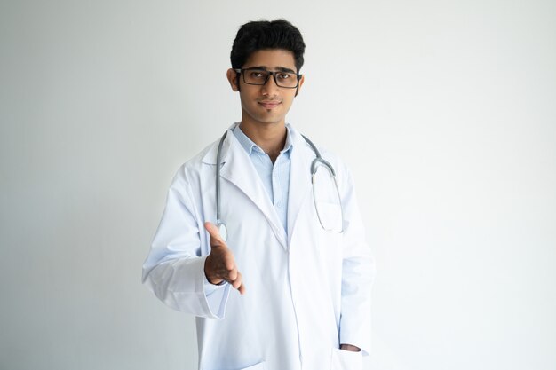Doctor de sexo masculino indio confiado serio que alcanza la mano para el apretón de manos y la mirada de la cámara.