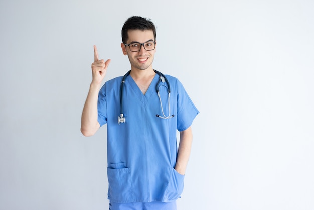 Doctor de sexo masculino joven sonriente que señala hacia arriba
