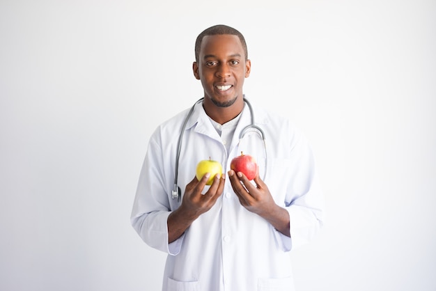 Doctor de sexo masculino negro sonriente que sostiene la manzana amarilla y roja.