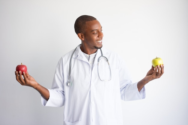 Doctor de sexo masculino negro sonriente que sostiene manzanas verdes y rojas.
