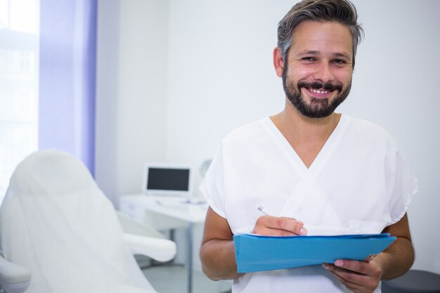 Doctor sonriente escribiendo en informes médicos en clínica