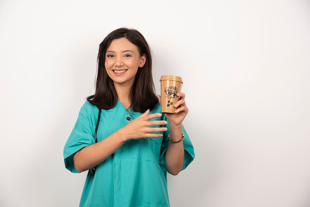 Doctor sonriente con estetoscopio sosteniendo una taza de café sobre fondo blanco.