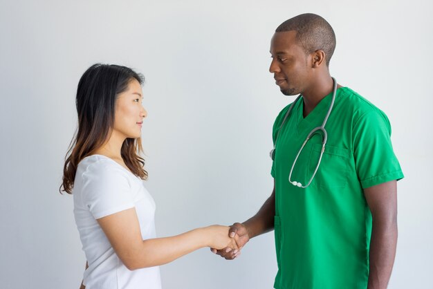 Doctor sonriente que saluda al paciente femenino joven con el apretón de manos.