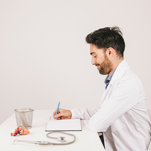 Doctor sonriente sentado en su escritorio y escribiendo