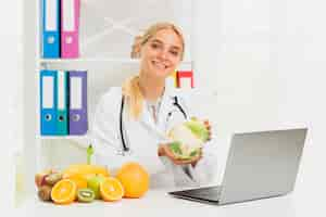 Foto gratuita doctor sonriente de tiro medio con laptop y coliflor