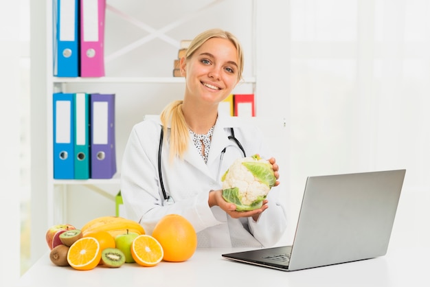 Doctor sonriente de tiro medio con laptop y coliflor