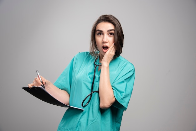 Doctor sorprendido en uniforme azul de pie en la pared gris.