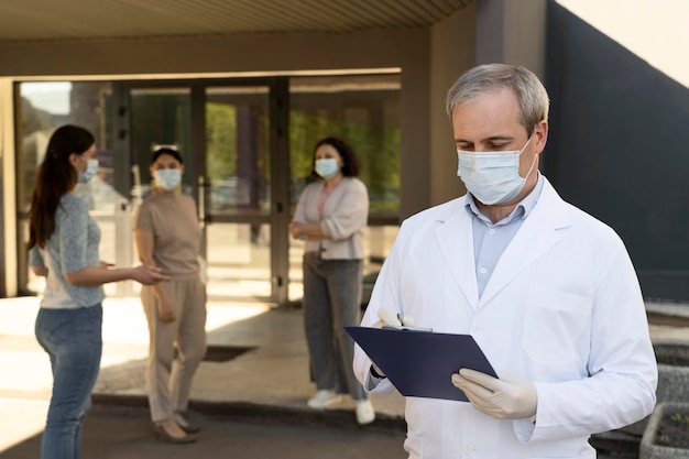 Doctor sosteniendo el bloc de notas en el centro de vacunación con pacientes al aire libre