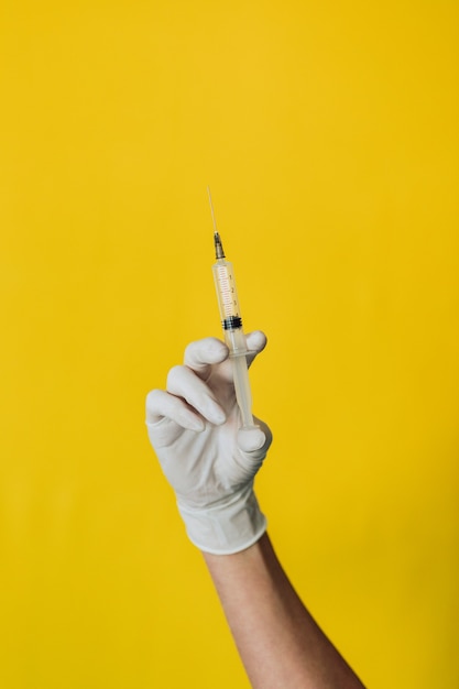 Doctor sosteniendo una jeringa sobre un fondo amarillo